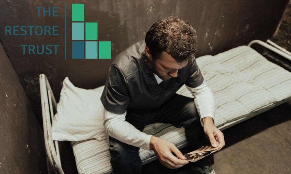 Image of a man in a prison cell, with The Restore Trust logo on.